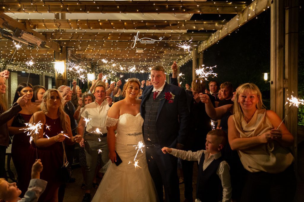 Julia Healey Photography A bride and groom stand together under a canopy of string lights, surrounded by guests holding sparklers at night.
