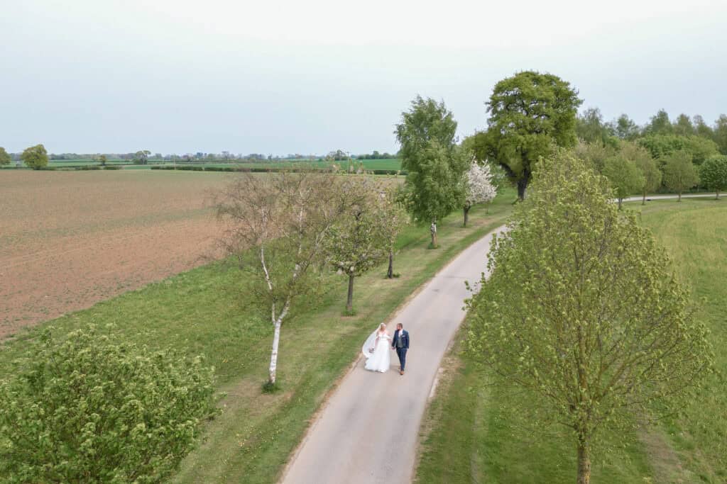 Bride and groom walking on tree-lined country road.