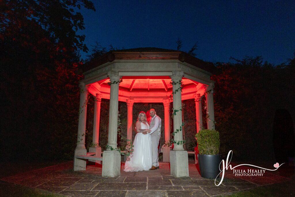 Couple under gazebo lit with red lights at night.