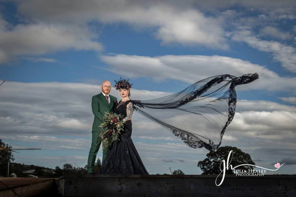 Couple in gothic wedding attire with dramatic veil.