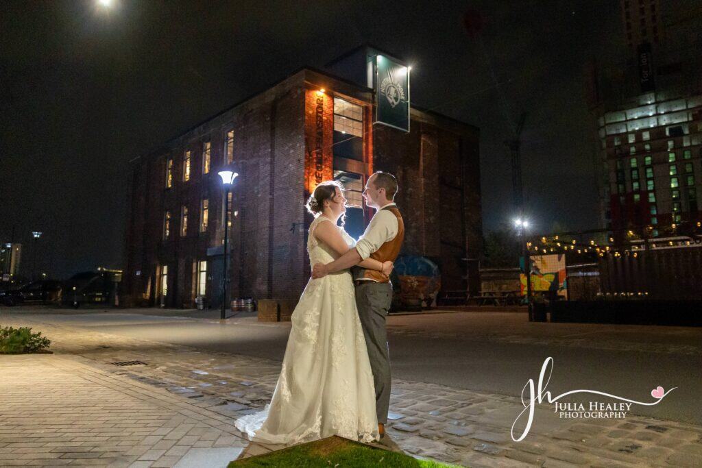 Couple embracing at night outside brick building.