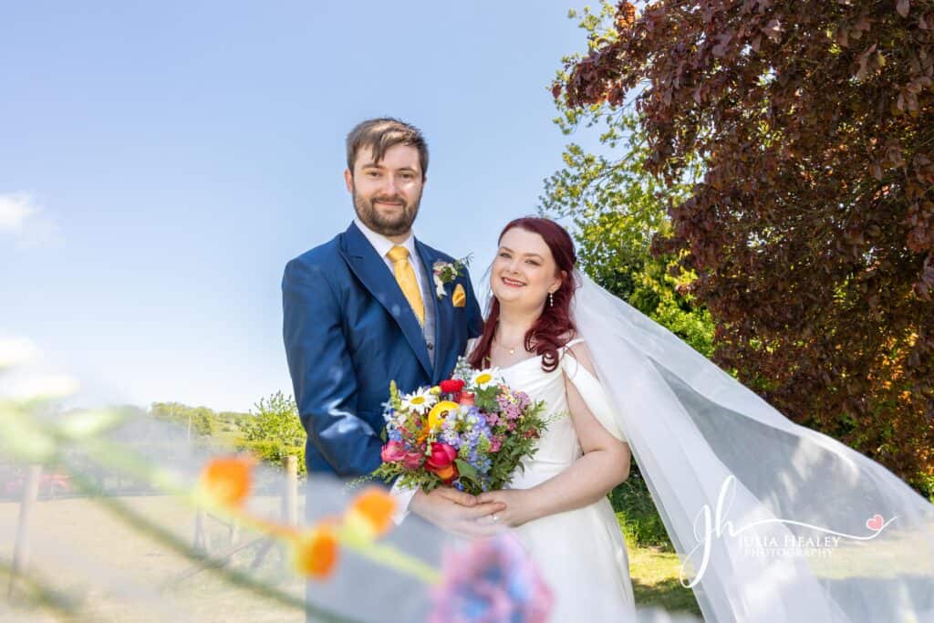 Bride and groom smiling outdoors with bouquet.