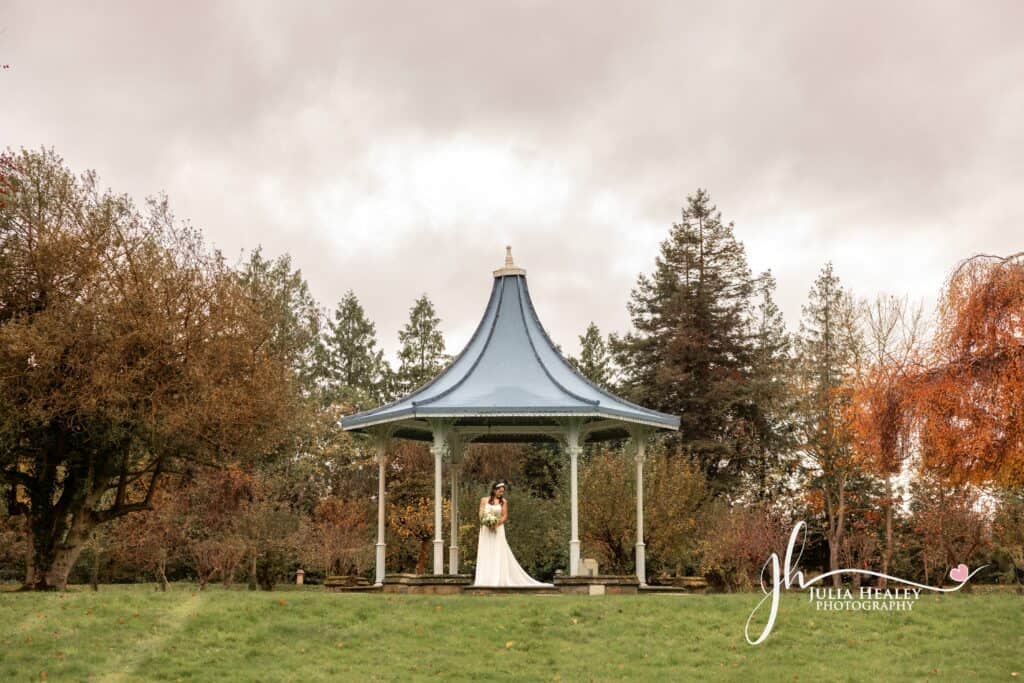 Bride in gazebo amidst autumn trees.