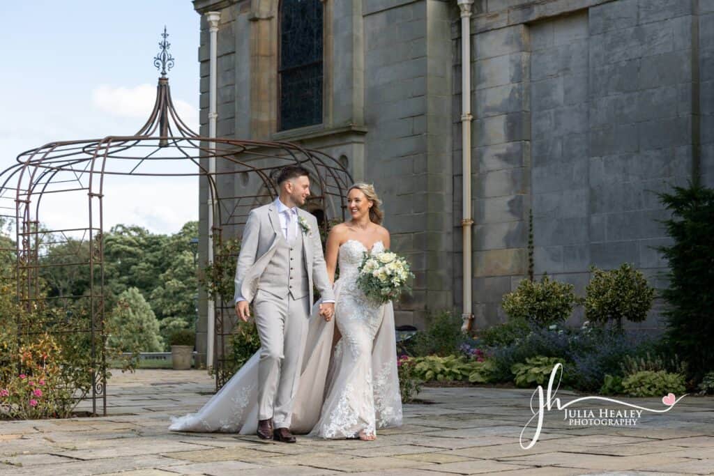 Bride and groom walking outside stone building.
